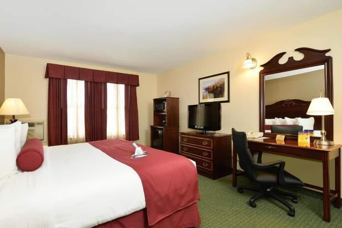 Une chambre d’hôtel équipée d’un lit, d’un bureau, d’une chaise, d’une télévision, d’une commode et d’un grand miroir.