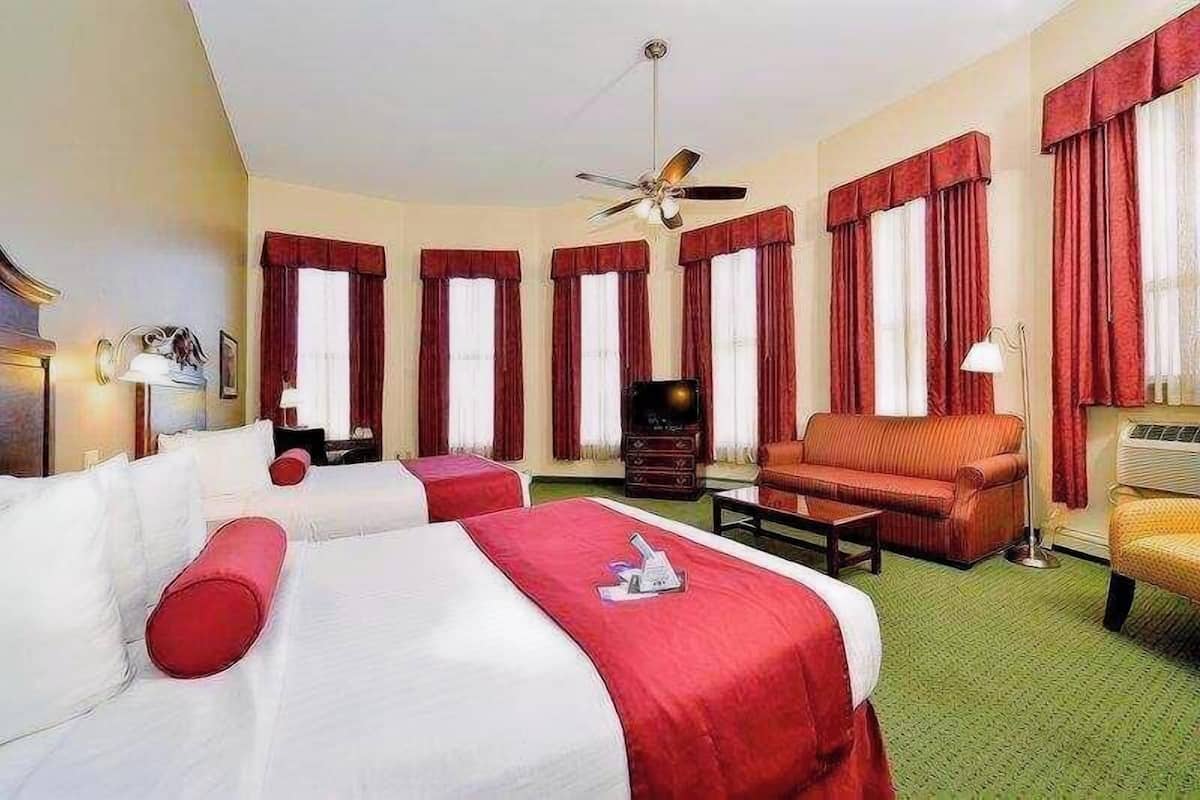 Une chambre d’hôtel avec deux lits, un canapé, une télévision et un ventilateur de plafond.