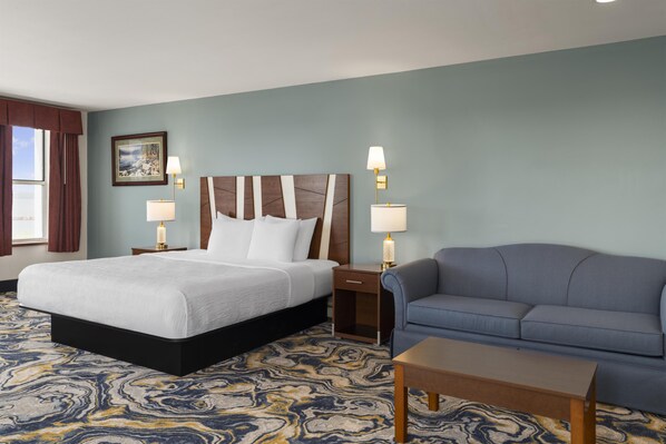 A hotel room with a large bed, a sofa, a small table, and two bedside lamps.