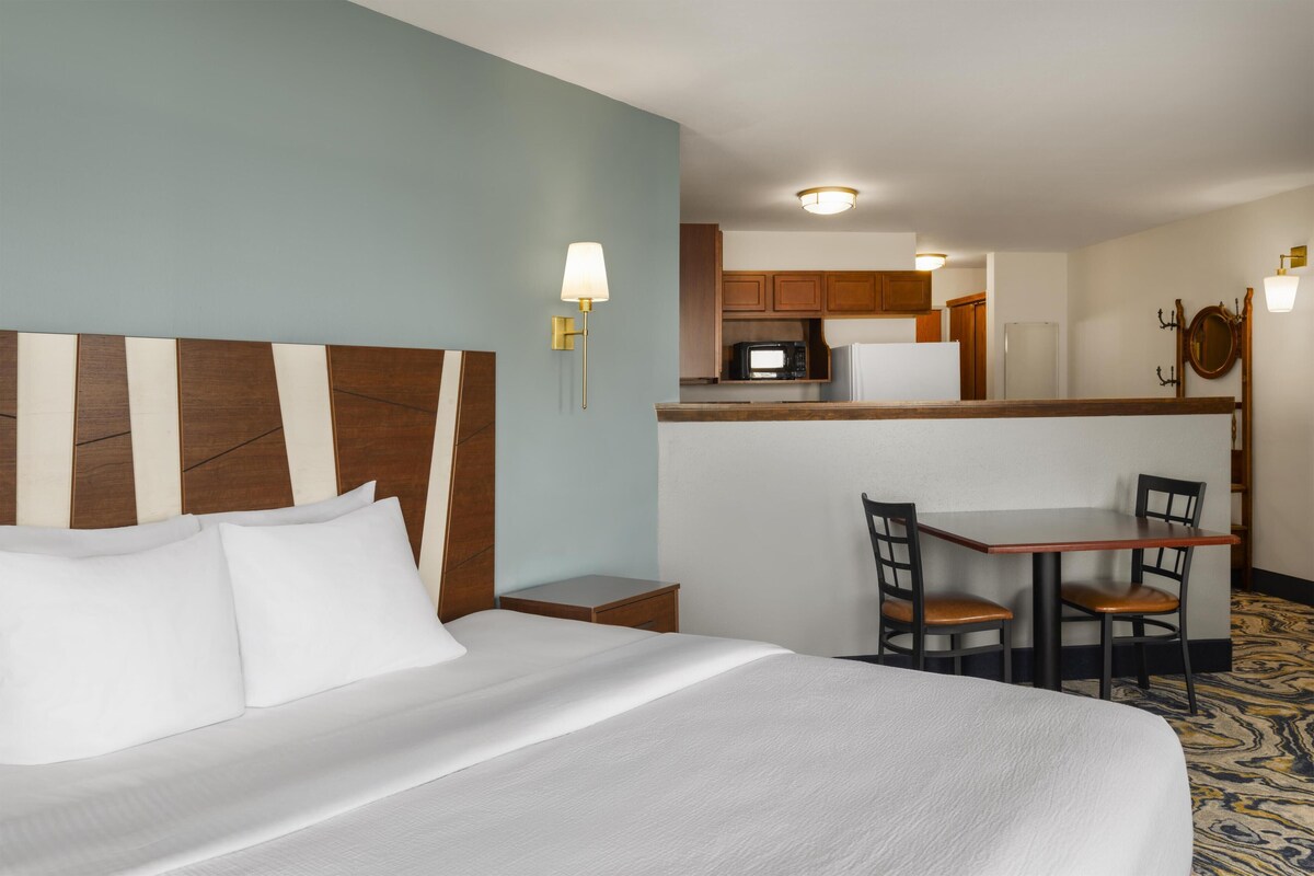 Une chambre d’hôtel avec un grand lit, une petite table à manger et, au fond, un coin cuisine.