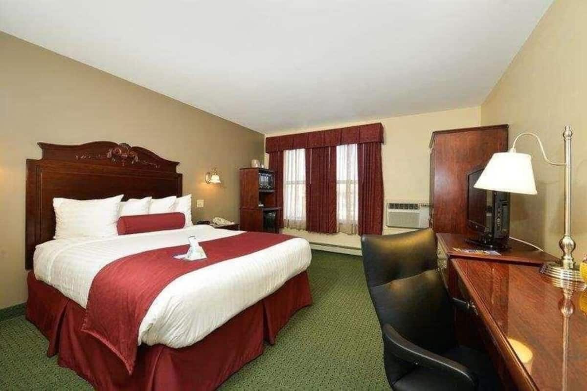 Une chambre d’hôtel avec un grand lit, un bureau avec une lampe, une chaise, un téléviseur et une fenêtre avec des rideaux.