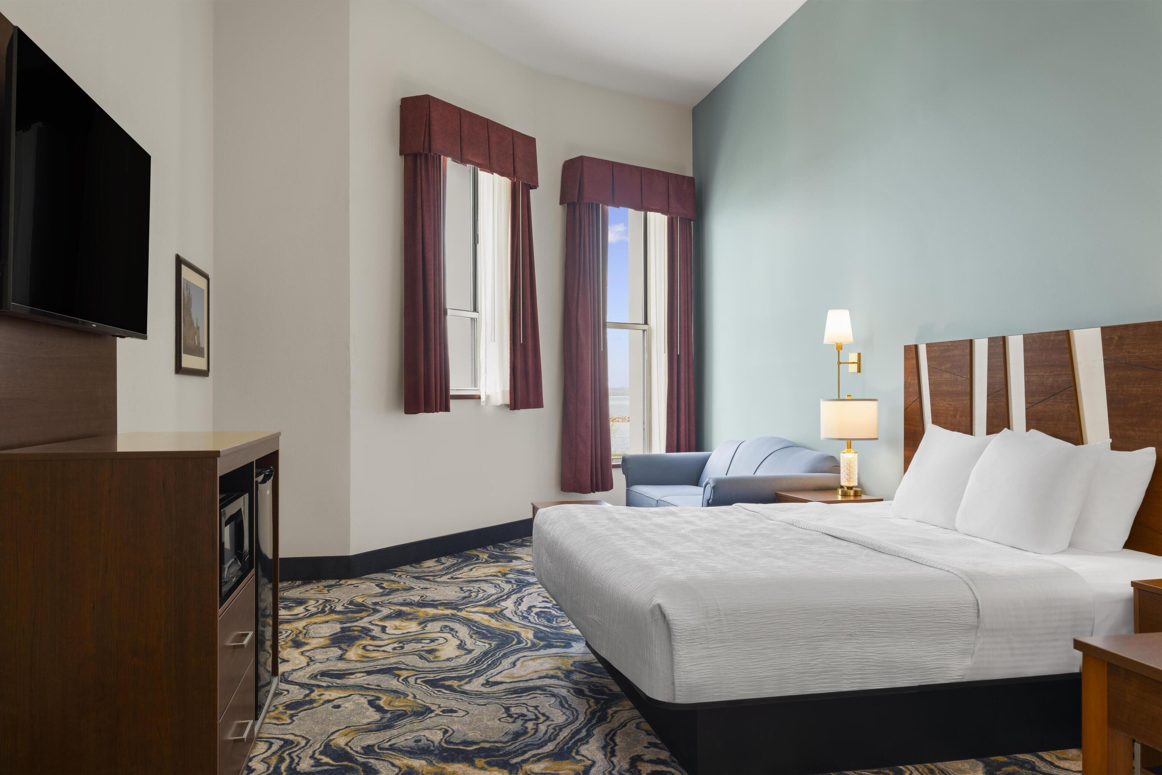 A hotel room with a bed, a desk, a television, and a window with curtains.