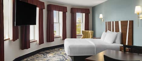 A hotel room with a bed, a desk, a chair, a television, and a window with curtains.
