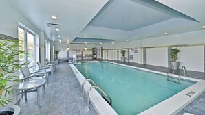 Une piscine intérieure à l’eau claire, entourée d’espaces aménagés pour s’asseoir et de plantes en pot.