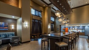 Un hall d’hôtel spacieux avec un bar central, des espaces aménagés pour s’asseoir et une cuisine moderne visible au fond.