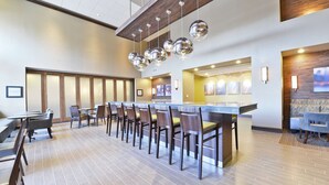 Un hall d’hôtel moderne doté d’un long comptoir d’accueil, de plusieurs espaces salon et d’un haut plafond orné de luminaires sphériques suspendus.