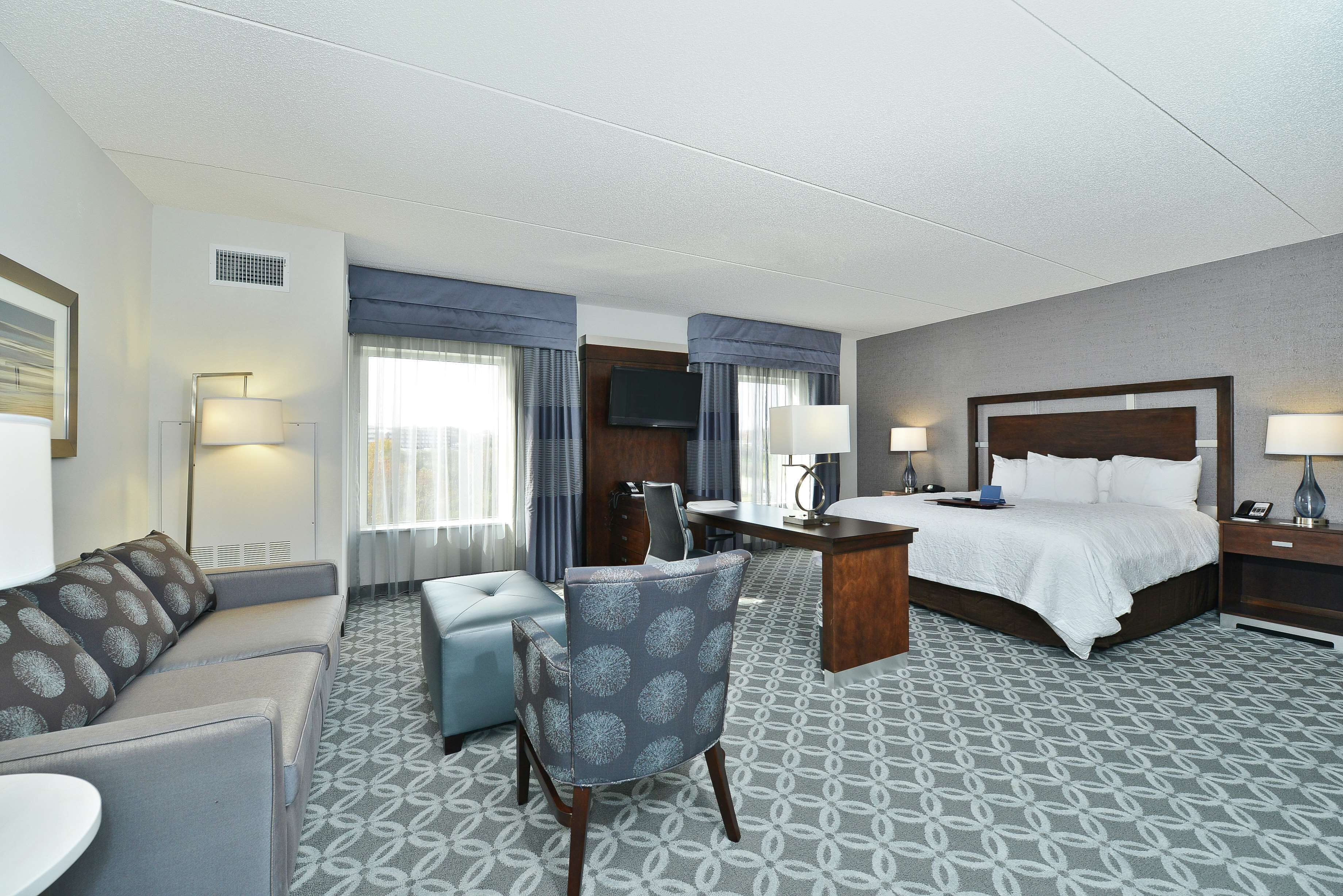 A hotel room with a bed, a desk, a chair, a sofa, and a TV.