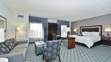 A hotel room with a bed, a desk, a chair, a sofa, and a TV.