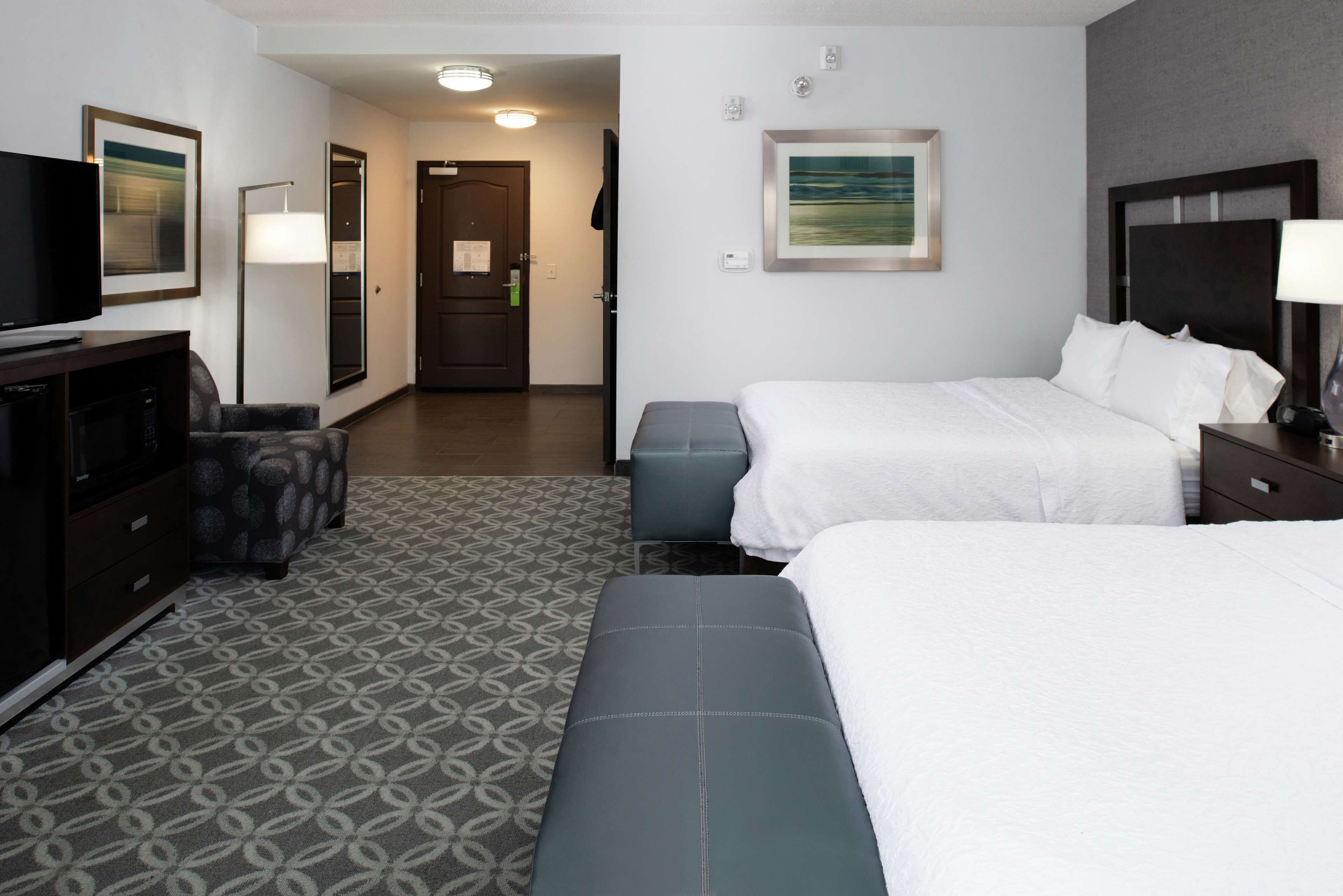 A hotel room with two beds, a desk, a TV, and a patterned carpet.