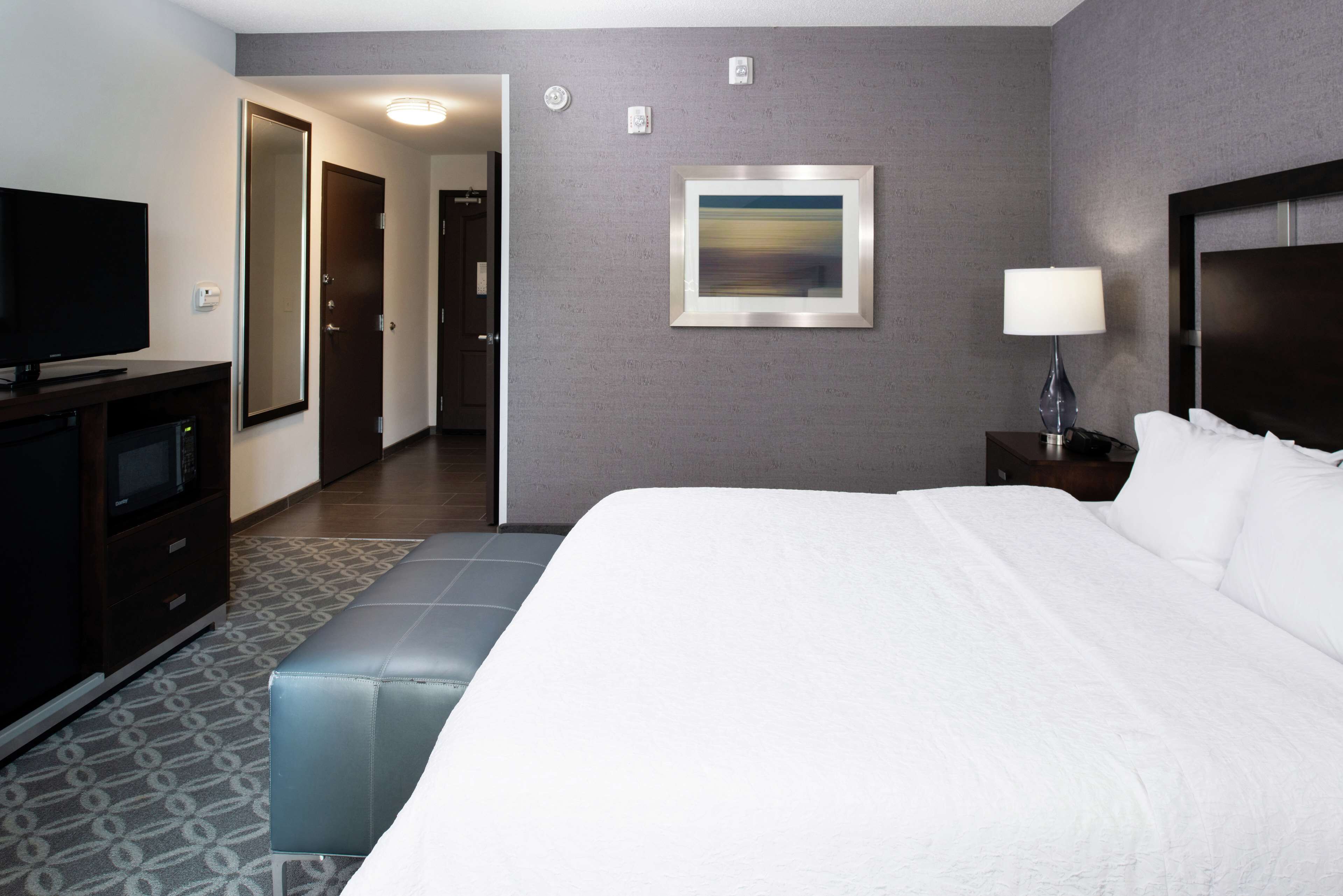A hotel room with a large bed, a television, a desk with a lamp, and a painting on the wall.