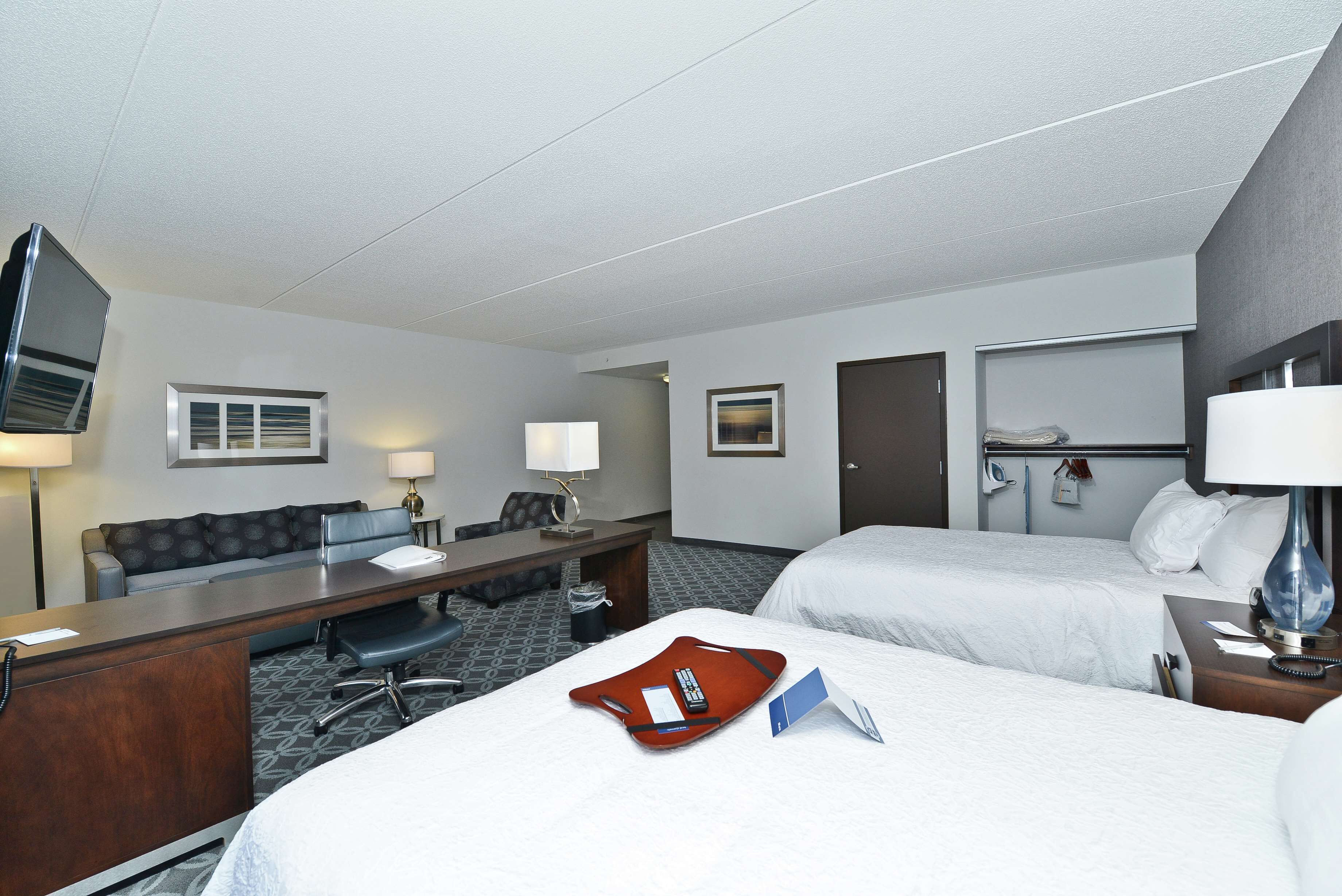 A hotel room with two beds, a desk, a chair, a TV, and a bathroom.