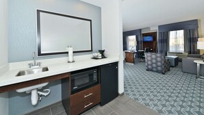 Une chambre d’hôtel équipée d’une kitchenette, d’un grand miroir, d’un téléviseur à écran plat et d’un coin salon agrémenté d’un tapis à motifs.