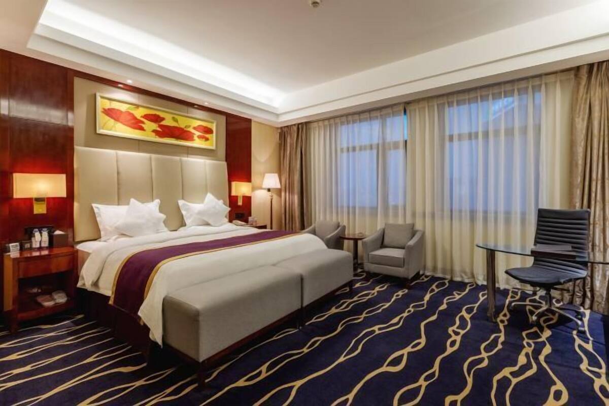 A hotel room with a large bed, a desk, a chair, and a window with curtains.