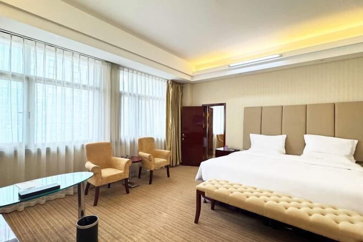A hotel room with a bed, two armchairs, a small table, a bench, and a door.