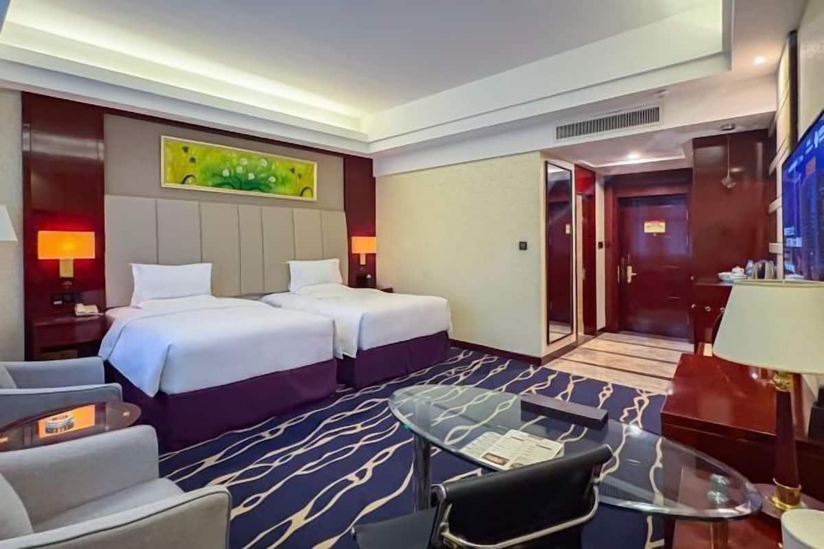 A hotel room with two beds, a glass table, a sofa, and a TV.