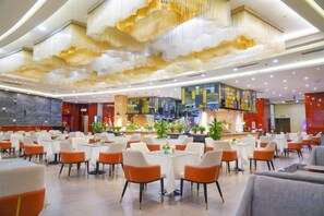 A spacious dining area with multiple tables and chairs, a central bar area, and a modern ceiling design.