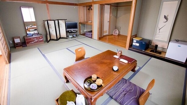 Une pièce de style japonais traditionnel, avec un sol recouvert de tatamis, une table en bois sur laquelle est disposé un service à thé et un téléviseur.