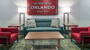 Habitación de hotel con sofá, dos sillones, una mesita de centro y un cartel en la pared que dice "gateway village - ORLANDO, quédate un rato".