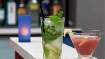 Two cocktails on a bar counter with a blurred background of bottles.