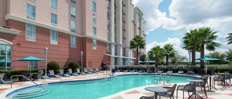 A hotel pool area with lounge chairs, umbrellas, and a swimming pool.