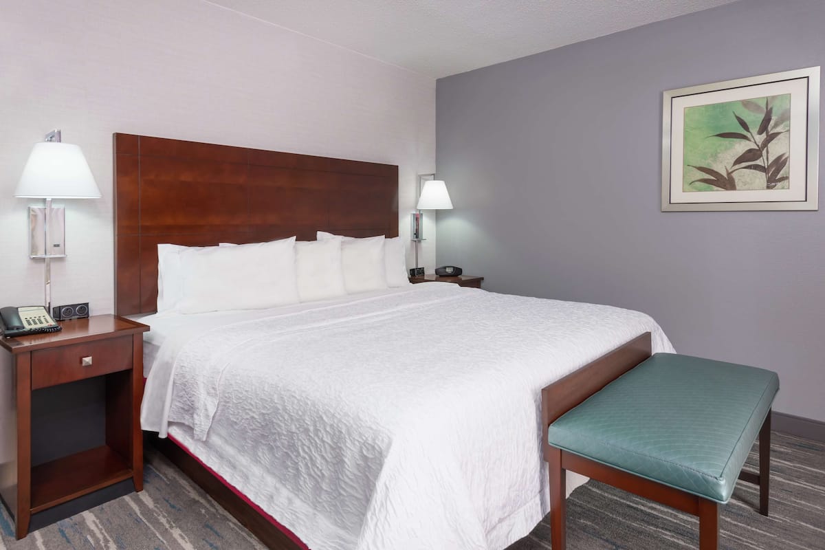 A hotel room with a large bed, a bedside table with a lamp, a phone, and a small table with a lamp.