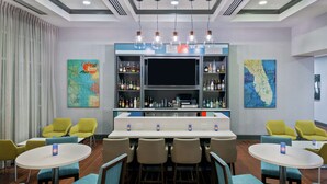 Una zona de bar con una barra larga, diversas opciones de asientos y una pantalla de televisión.