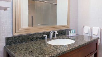 A bathroom with a granite countertop sink, a large mirror, and a towel rack.