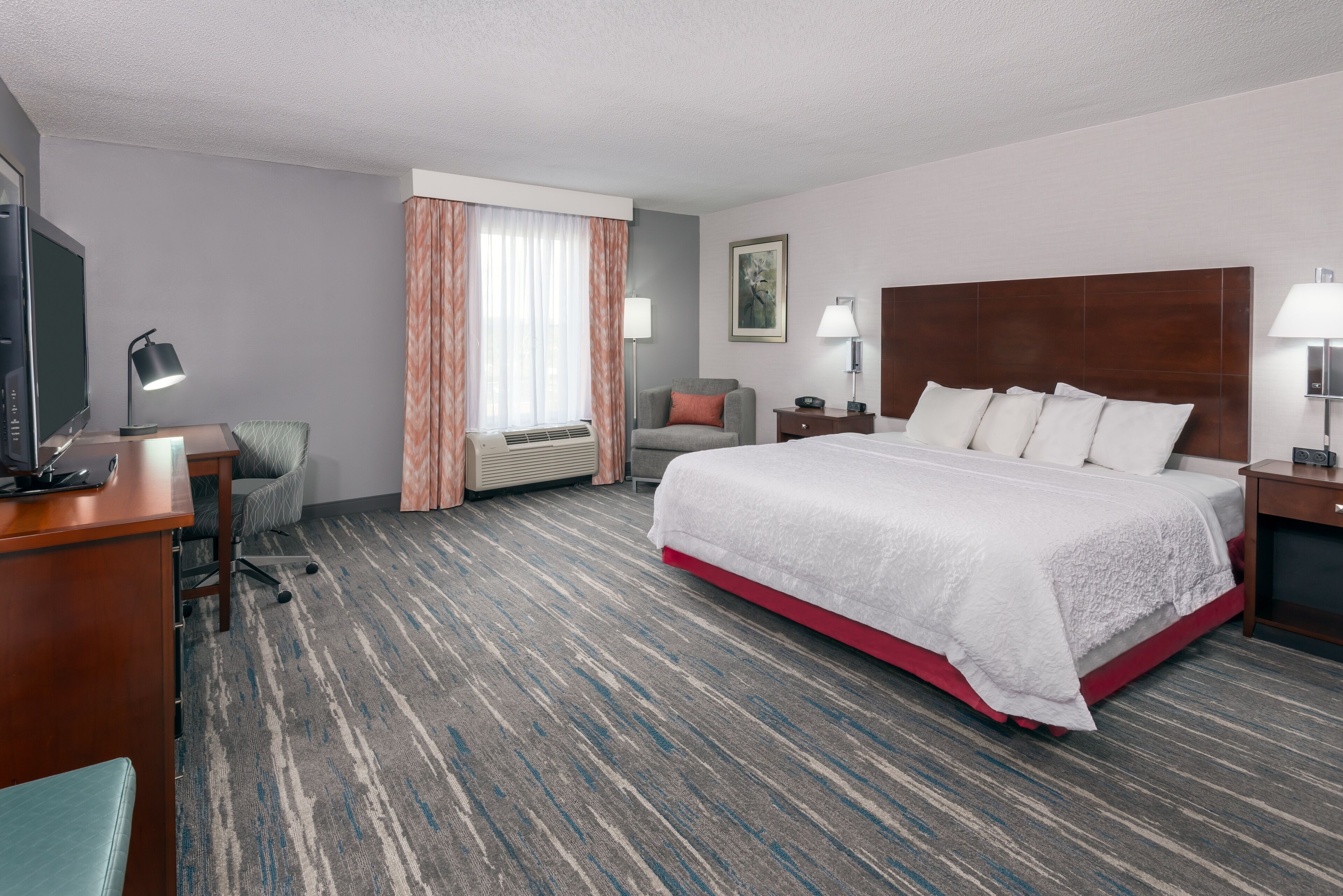 Een hotelkamer met een groot bed, een bureau met een computer, een stoel, een televisie en een raam met gordijnen.