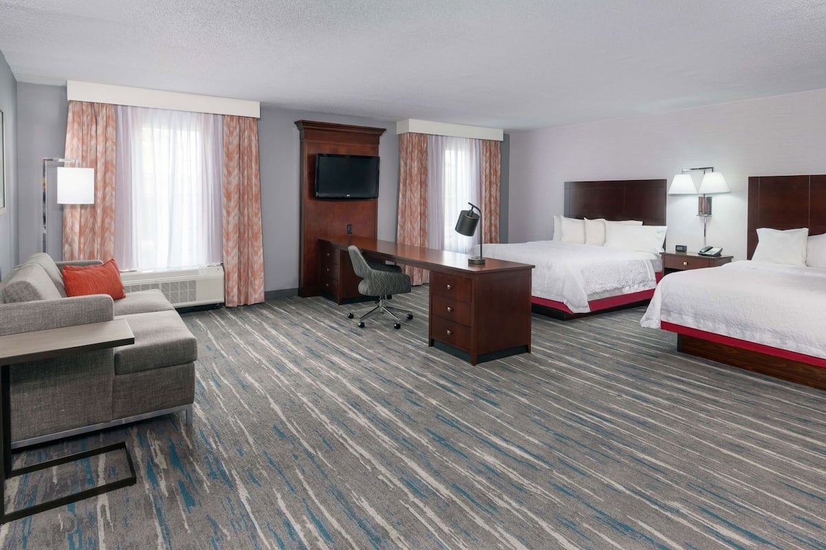 A hotel room with a desk, two beds, a sofa, a TV, and a lamp.