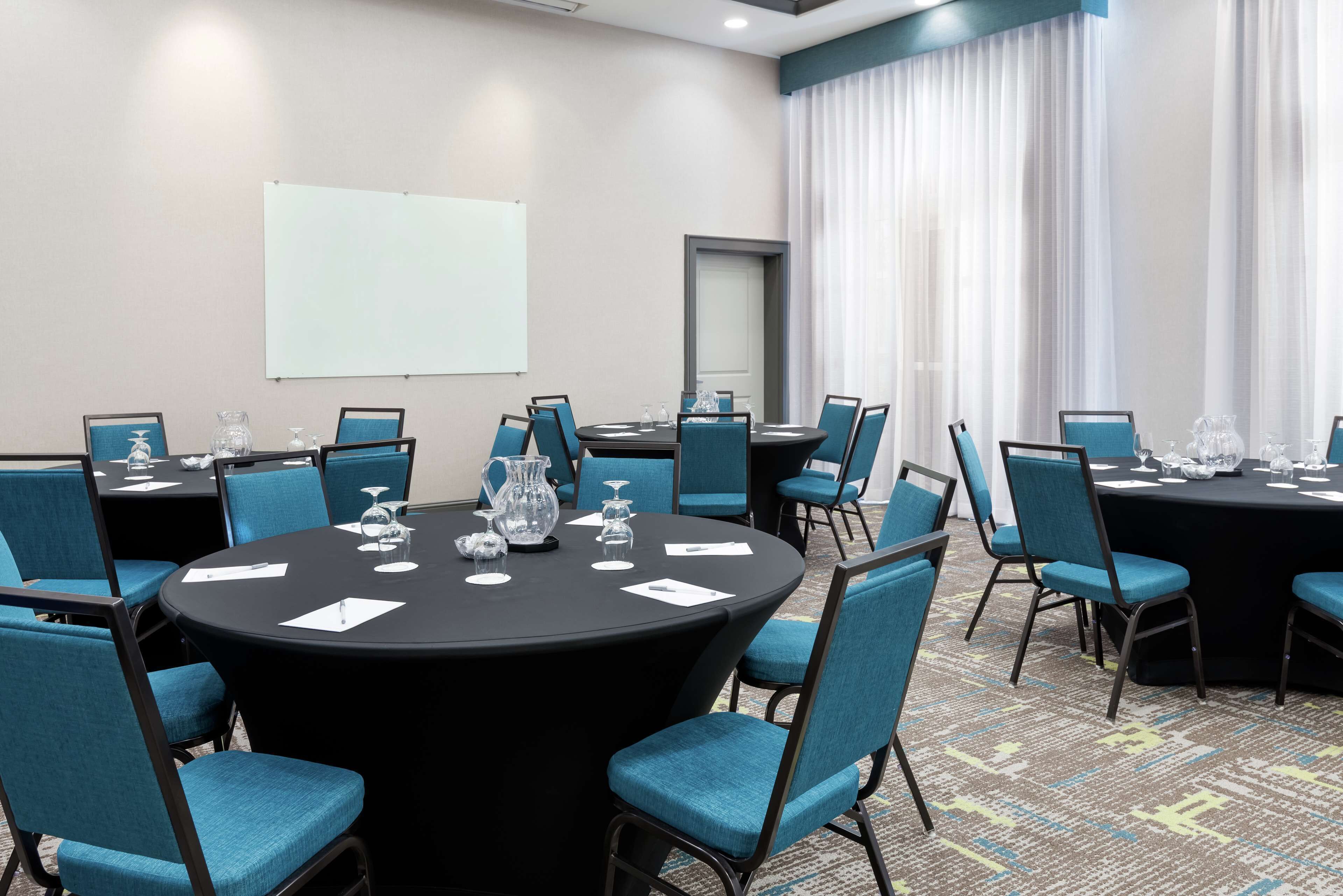 A conference room with round tables, blue chairs, and a projector screen.