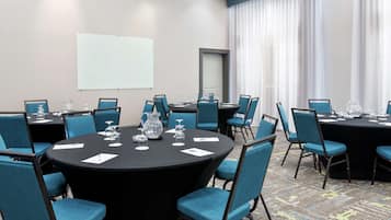 A conference room with round tables, blue chairs, and a projector screen.