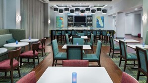 Un hall de hotel con mesas redondas, sillas, una zona de bar y una pantalla grande.