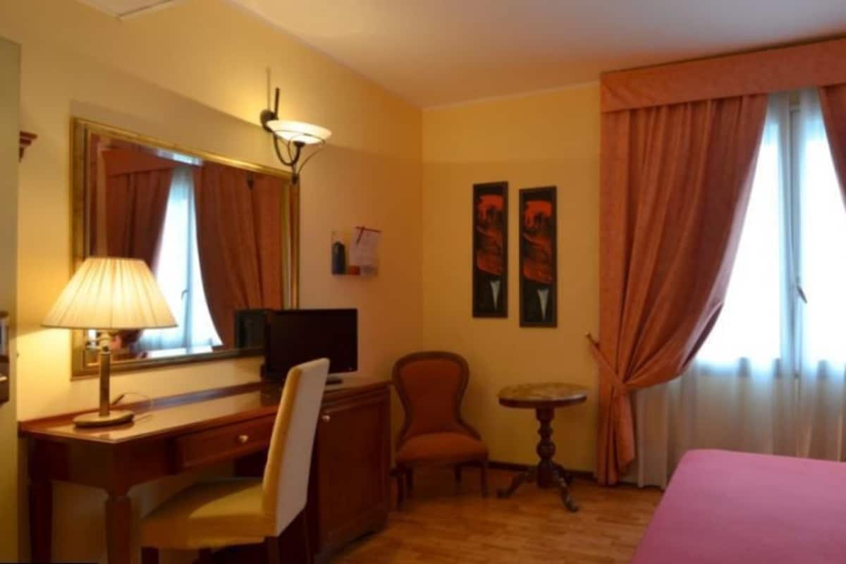 A hotel room with a bed, desk, chair, and a small table.