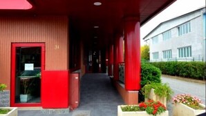 The entrance of Hotel Vazzana with a red facade and a covered walkway leading to the entrance. - Hotel Vazzana (Volpiano)