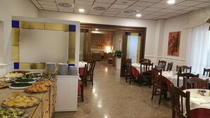 A dining area with multiple tables and chairs, a buffet with various dishes, and a hallway leading to a seating area. - Hotel Vazzana (Volpiano)