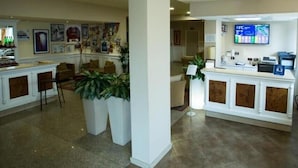 A hotel lobby with a reception desk, seating area, and a wall with framed pictures. - Hotel Vazzana (Volpiano)