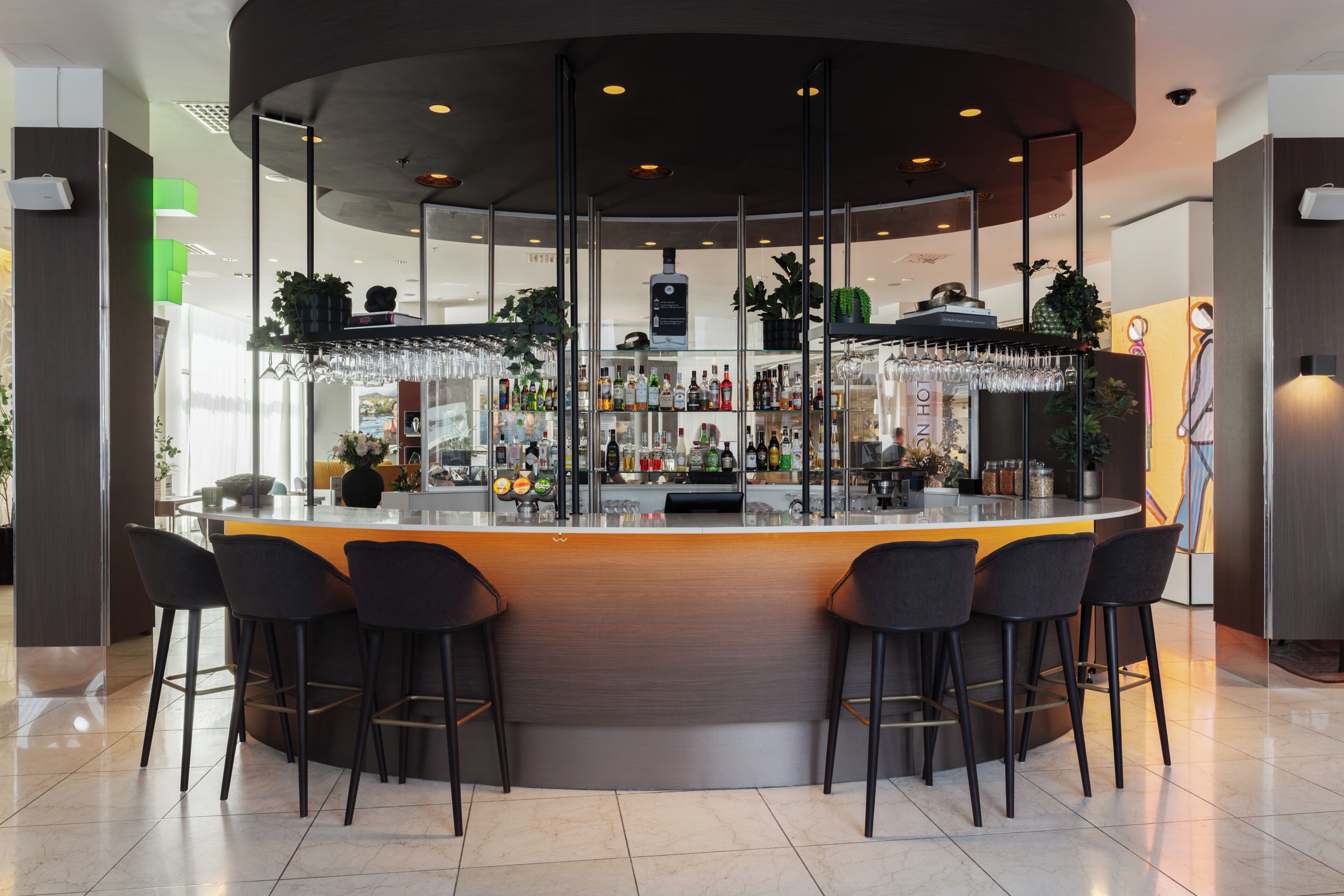 Zona de bar moderna con una barra curva, taburetes y una variedad de botellas y vasos.