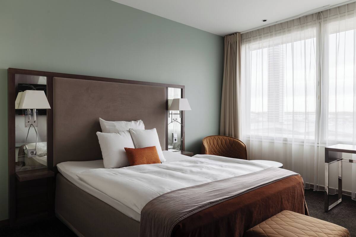 A hotel room with a large bed, a desk, and a chair.