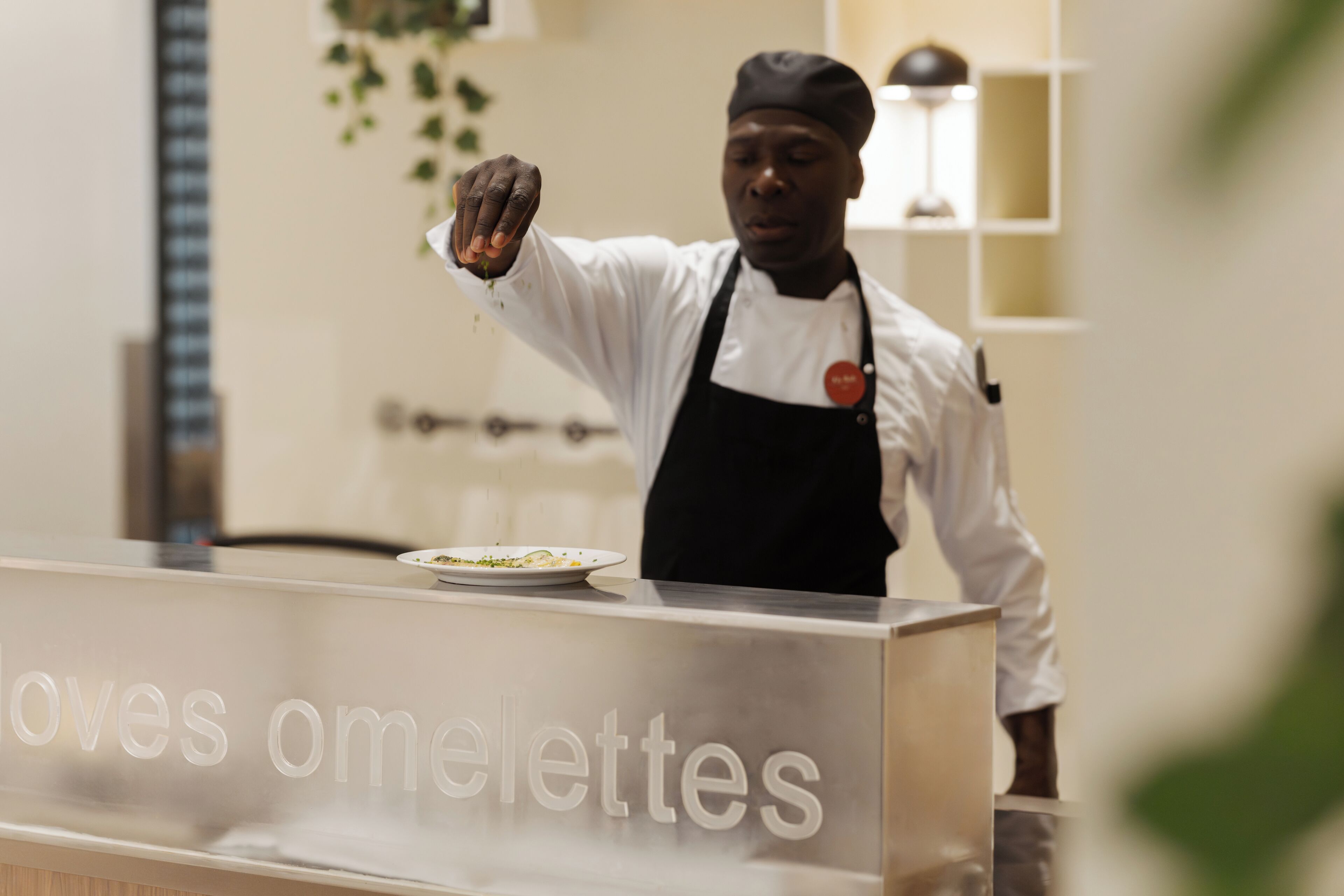 A chef in a white shirt and black apron standing behind a counter with the text 'omelettes' visible.