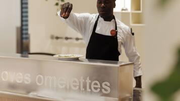 A chef in a white shirt and black apron standing behind a counter with the text 'omelettes' visible.