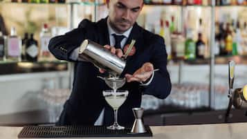 Un cantinero preparando una bebida en la barra, con estantes llenos de botellas al fondo.