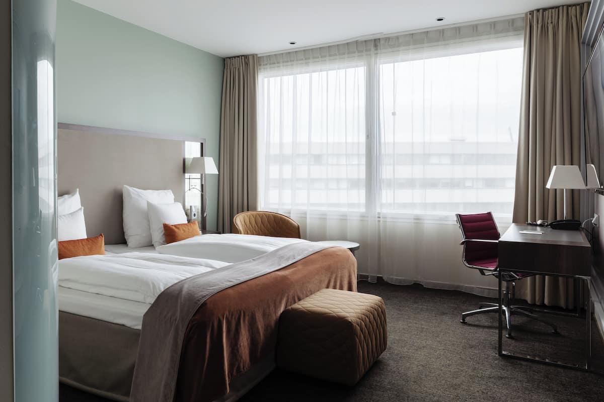 A hotel room with a bed, a desk, a chair, and a large window.