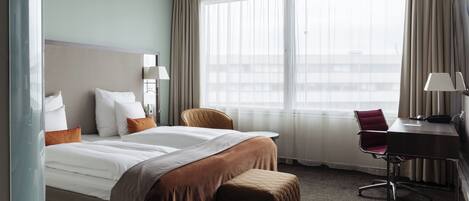 Una habitación de hotel con cama, escritorio, silla y un ventanal grande.