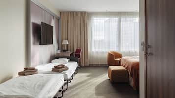 Habitación de hotel con dos camas, televisión, escritorio con lámpara, una silla y un ventanal grande con cortinas.
