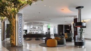 A modern hotel lobby with a reception desk, seating areas, and a decorative plant arrangement.