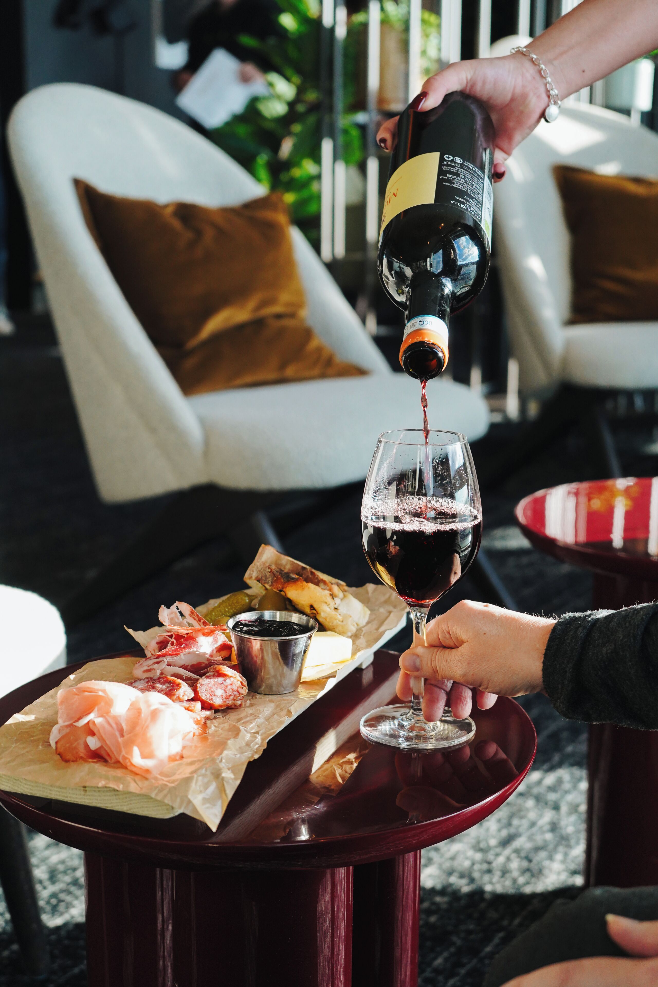 A person pouring wine into a glass on a table with food and a bottle.