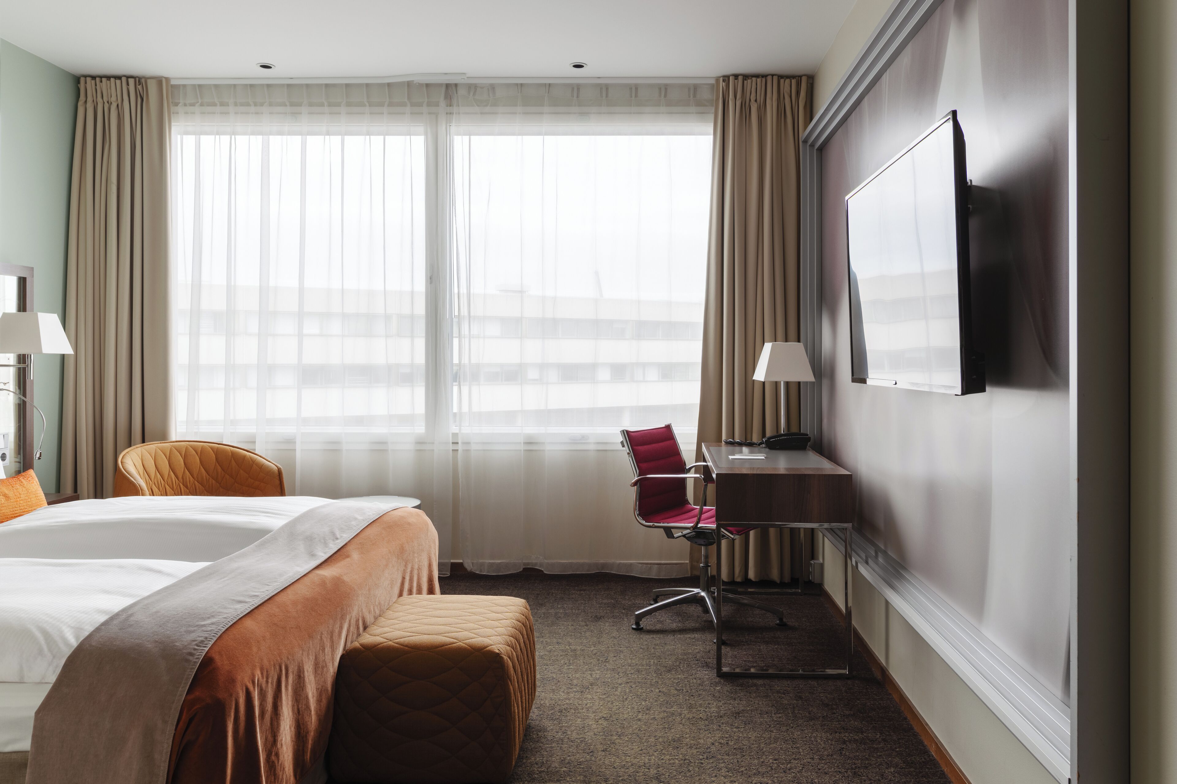 A hotel room with a bed, a desk, a chair, and a TV on the wall.