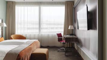 A hotel room with a bed, a desk, a chair, and a TV on the wall.
