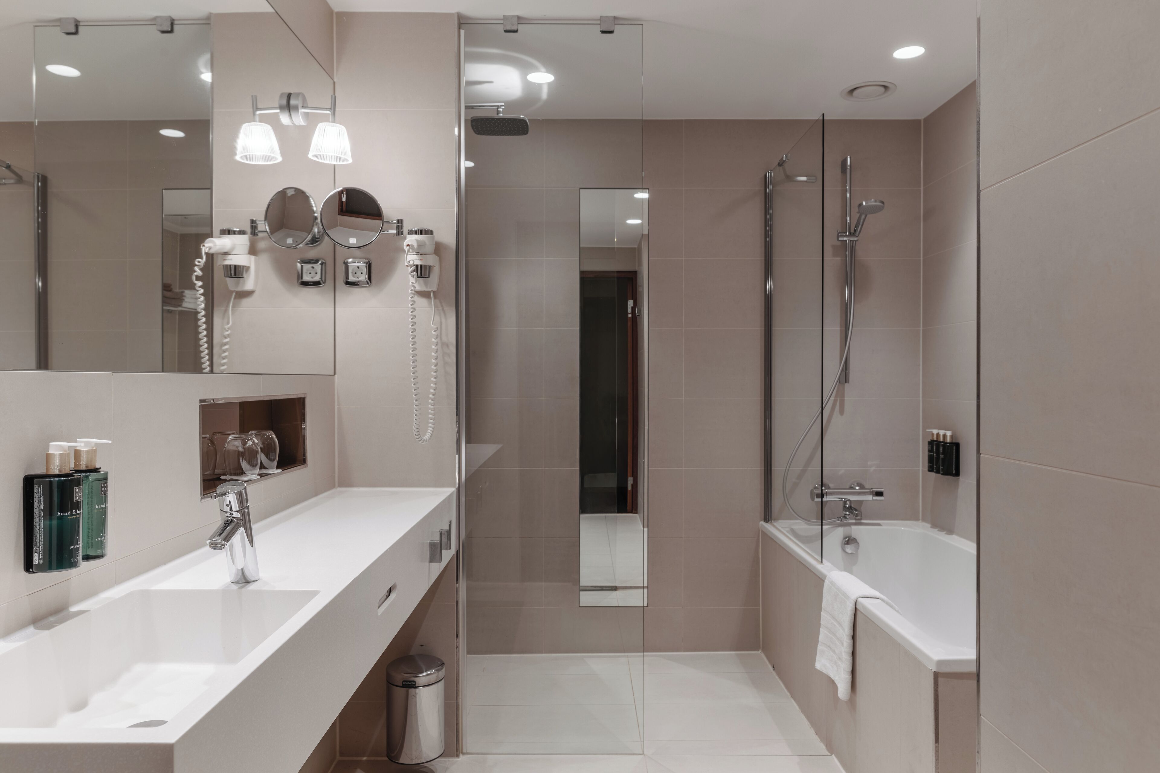 A modern bathroom with a large mirror, two sinks, a shower, and a toilet.