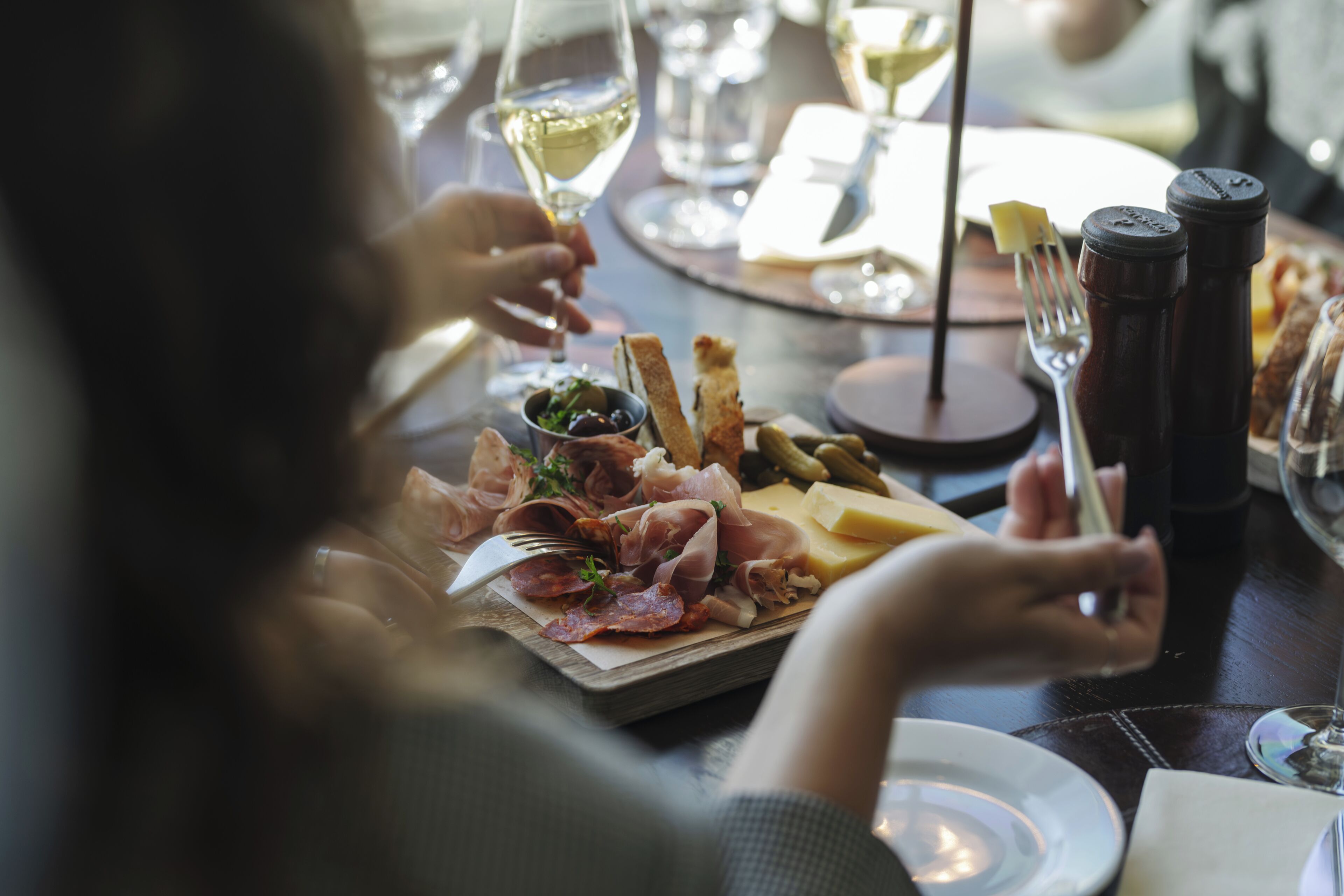 Un tavolo imbandito con diversi cibi, tra cui carni, formaggi e pane, insieme a bicchieri da vino e posate.